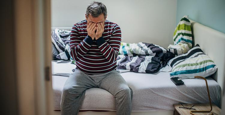 Man sitting on bed with head in his hands