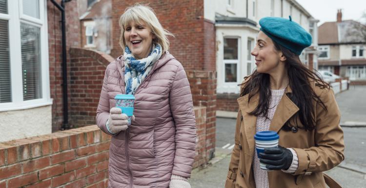 2 women walking outside talking and holding coffee